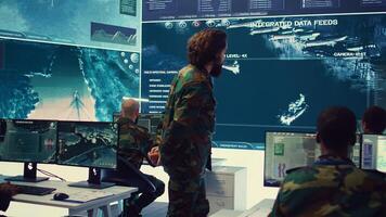 Staff sergeant briefing his army troops crew with details of a new mission, operating command center devices to monitor radar CCTV footage and provide information to people in the field. Camera B. photo