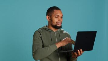Happy man adding payment method on website using laptop, delighted to take advantage of promotions, studio background. Person thrilled to do internet shopping, typing credit card data, camera A photo