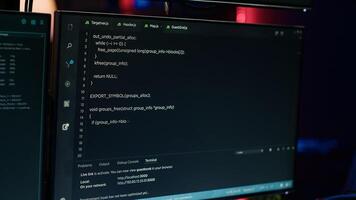 Extreme close up of software interface on PC screens showing lines of code running in empty criminals den. Hacking malware programming script on displays in underground base, handheld camera shot photo