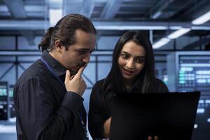 IT experts in server hub doing brainstorming, finding ways to ensure data remains shielded from potential threats. Employees chatting, safeguarding data center against unauthorized access using laptop photo