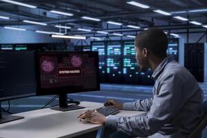 African american man in server hub trying to protect hardware from hacker stealing sensitive information. Data center workplace engineer struggling to erase virus after seeing security breach alert photo