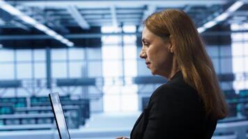 System administrator in data center typing on laptop, running error checking utilities to fix problems. Woman in server hub looking for network issues affecting rigs using notebook device, camera A photo