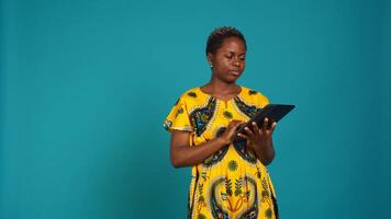 Happy positive adult navigating on online webpages in studio, using portable gadget to browse things on internet connection. Woman in traditional ethnic attire poses against background. Camera B. photo