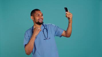 Male nurse using mobile phone to take selfies during hospital job shift break. Healthcare worker using smartphone to take pictures of himself, isolated over studio background, camera B photo