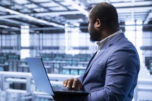 Programmer in data center implementing backup solutions to protect against infrastructure data loss using laptop. Modern workplace IT professional resolving technical issues using notebook photo