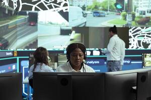 African american call center dispatcher sends gps coordinates of new routes to couriers in the field, helping to deliver orders in time. Employee works on express shipping service, CCTV footage. photo