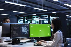 Team of technicians doing maintenance on green screen computer in server hub used for artificial intelligence workloads. Teamworking employees inspecting neural network data center with mockup PC photo