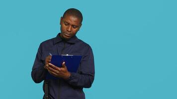 Security guard holding clipboard, taking notes, receiving orders during protection job shift. Portrait of bodyguard using pen to write informations received, studio background, camera A photo