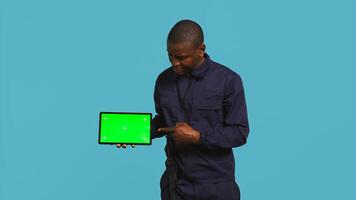 Portrait of security agent presenting chroma key tablet and securing assigned post, studio background. Guardian points finger to isolated screen device while handling security breaches, camera B photo