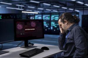 Technician in server hub doing face palm gesture, trying to protect hardware from hacker stealing information. Upset data center employee stressed by security breach alert caused by virus photo