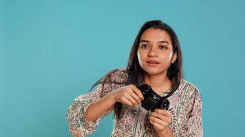 Focused woman playing videogames with motion controlled joystick, studio background. Indian gamer participating in online multiplayer racing game using gyroscope function on gamepad, camera B photo