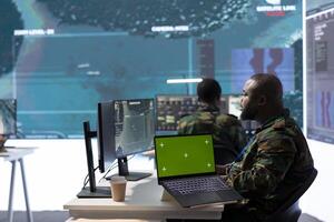 Military IT specialist in command center working on collecting field data, process real time surveillance footage and imagery for successful defense operation. Using isolated mockup display on pc. photo