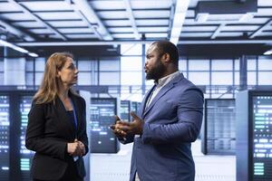 Colleagues doing brainstorming in server hub after installing storage units. IT staff member talking in data center, doing maintenance after replacing mainframes components photo
