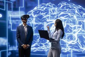 Engineer wearing VR headset looks at hologram of artificial intelligence human brain simulation, assisted by colleague using laptop. Team of developers interacting with AI visualization photo