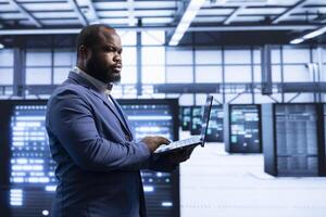 System administrator in data center implementing backup solutions to protect against data loss using laptop, ensuring efficiency. High tech facility worker resolving technical issues using notebook photo