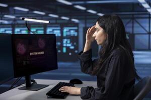 Engineer in server hub frightened by hacking attack on computers targeting sensitive user data. Afraid woman panicking, trying to save data center from unauthorized access photo