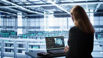 Engineer in data center using artificial intelligence computing simulating human brain thought processes in computerized model. Employee works on laptop with AI machine learning algorithms, camera B photo
