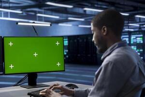 Technician in server hub ensuring data remains shielded from potential threats using green screen PC. Employee safeguarding data center hardware against malicious access with mockup computer display photo