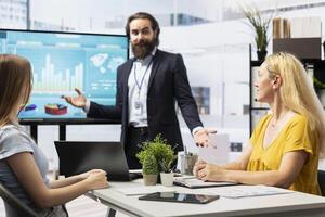 Financial advisor showing statistical graphs on big screen to customers, analyzing market trends to optimize income. Family members checking investment plan on display made by consultant photo