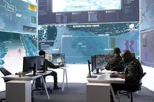Army staff in a high tech control room managing crucial defense information, gathering live surveillance data to maintain security protocols. Military crew members working on reconnaissance. photo