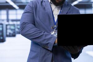 Admin walking in data center, using laptop to configure network infrastructure such as routers, switches and firewalls. Close up of IT expert in server hub looking for technical issues using notebook photo