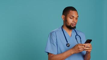 Male nurse using mobile phone to scroll on social media feed during hospital job shift break. Healthcare worker using smartphone to text friends, studio backdrop, camera A photo