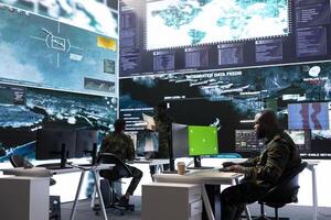 IT expert collecting real time information next to isolated chroma key screen, high tech military gear in command post. Soldier processing intelligence for field operations and strategic missions. photo