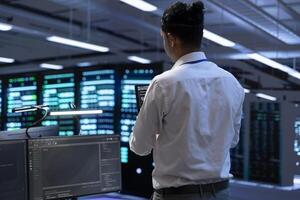 Engineer using tablet to troubleshoot hardware and software issues in server hub. IT specialist implementing and maintaining server and network infrastructure in data center photo