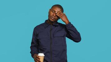 Tired security guard drinking coffee cup to stay awake, being tasked with preventing criminals. Portrait of weary bodyguard sipping caffeinated beverage during night shift, studio background, camera A photo