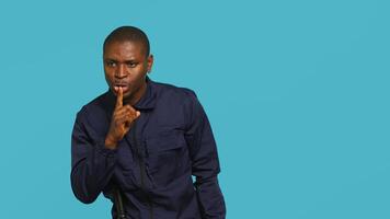 Security guard doing shush sign gesturing with finger, preventing public access in restricted area. Portrait of stern bodyguard urging people to keep quiet, studio background, camera A photo