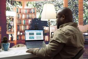 Enterprise owner studying financial reports and infographics at home office, working on developing business strategies and objectives. Analyst reviews market dynamics and progress. photo