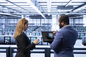 Teamworking colleagues using AI software on laptop, programming in AI data center. IT staff members in high tech server hub facility upgrading artificial intelligence systems photo