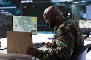 Military professional in a mission control center monitors satellite data feeds, communicating real time information for strategic missions in a base of operations with big screen. photo