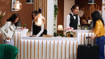 Young customer approaching front desk in hotel lobby, preparing for check in process after long flight. Asian staff greeting guest at reception, discussing about room reservation and facilities. photo