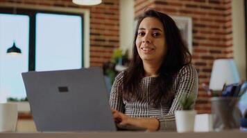 Portrait of cheerful freelancer checking her emails on notebook device while at computer desk. Self employed woman inputting data on laptop in bright cozy apartment office, solving tasks photo
