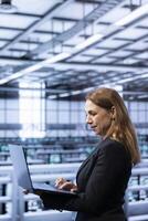 Data center system administrator ensuring safety and security of database using laptop. IT staff member in server farm preventing unauthorized access posing risks for company photo
