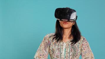 Indian woman wearing virtual reality headset, doing swiping gestures. Technology enthusiast using high tech futuristic modern VR gadget, isolated over studio background, camera B photo