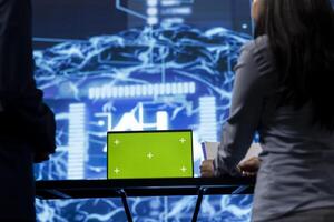 Green screen tablet used by computer scientists in startup doing advancements in AI field. Close up shot of employees working on mockup device in workspace featuring artificial intelligence systems photo