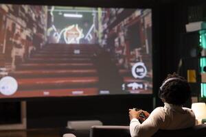 Gamer using headphones microphone to discuss with teammates while playing science fiction game on large smart TV. Player in apartment entertained by SF videogame on console, using joystick controller photo