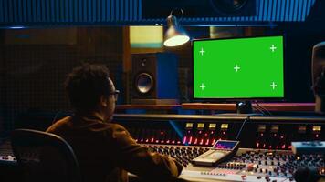 African american music producer working with greenscreen on pc, using mixing console to do mix and master in control room. Audio technician recording tracks with knobs and switchers. Camera A. photo