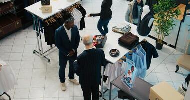 Senior designer teaching his apprentice to match ties on elegant suits, presenting the color mixing theory to his pupil. African american man trying to learn basics in fashion industry. Camera B. photo