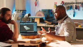 Carpenter looking over blueprints schematics on laptop in CAD software with apprentice. Woodworkers designing custom 3D furniture on notebook in studio, preparing for client order, camera A photo