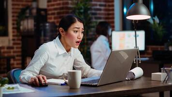 Asian employee gasping, shocked by negative response received from customer while discussing business matters over email. Worker wincing while looking at laptop screen, feeling disappointed photo