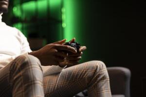 Man holding controller in green neon illuminated apartment, playing videogames. Gamer on couch using joystick to participate in PvP online multiplayer game on console system, relaxing and having fun photo