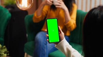 Woman checking greenscreen display on smartphone layout, passing time in lounge area at hotel. Asian tourist sitting on sofa with phone running isolated chromakey template on screen. photo