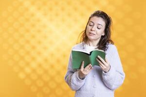 Jolly woman turning page on book, enjoying story, conveying joy of reading concept, studio background. Radiant geek reading hardcover novel, showing appreciation for literature photo