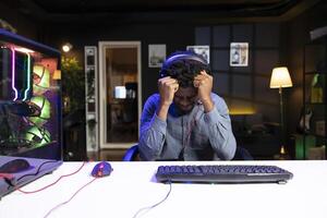 Upset gamer putting head in hands in frustration after getting game over message while playing videogame. Man feeling depressed after losing while playing on computer desktop photo