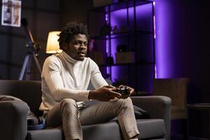 Player playing videogames on console late at night in purple neon lit room, struggling to stay awake. Man using gamepad controller to try and finish game level before going to sleep, feeling sleepy photo
