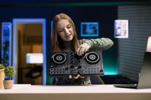 Cheerful young artist filming DJ mixing tutorial in home studio, showing examples of sampling on sound controller to viewers. Happy gen Z entertainer showing modern musical equipment to audience photo