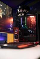 RGB lit parts on opened gaming PC tower next to keyboard, stereo speakers, display and high tech VR headset in empty apartment. Computer with modern hardware, monitor and virtual reality glasses photo